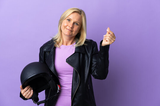 Middle Age Woman Holding A Motorcycle Helmet Isolated On Purple Background Making Money Gesture