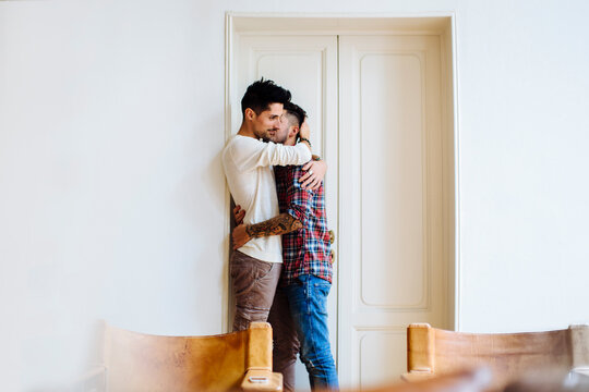 Young men hugging near door in cozy apartment