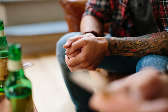 Faceless tattooed man on sofa near bottles of beer