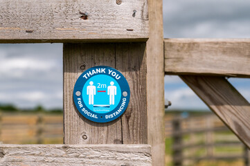 Sign attached to a wooden gatepost thanking visitors for remaining 2 metres apart and social...