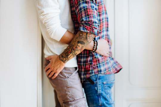 Crop gay couple hugging near door in cozy room