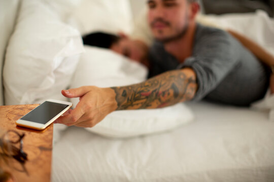 Young gay taking smartphone from bedside table