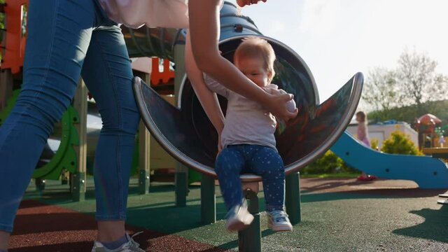 Mother teaches her child to get up from the baby slide. Baby girl gets up and funny falls to the ground. Real time. The concept of children's education.