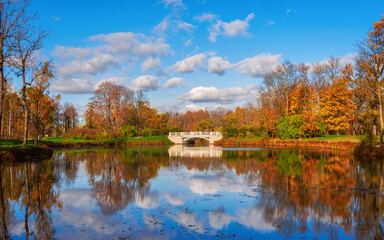 Fototapeta na wymiar Picturesque autumn landscape with a pond. Beautiful autumn landscape with old stone bridge, red trees and reflection on the lake. Alexander Park, Tsarskoe Selo.