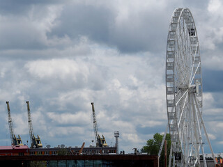 ferris wheel on the river bank against the background of blue sky with clouds side view