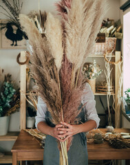Unrecognizable Woman Holding Pampas in her Hands at Studio with Dry Flowers and Plants.
Young...