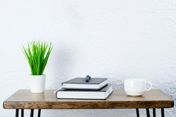 Notepad and books and pen on the table. Desktop. Green flowerpot in a white pot. A cup of coffee. Office.