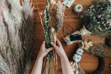 Top View of Female Hands Making Everlasting Bouquet of Dried Flowers at Wooden Table with Bunch of...