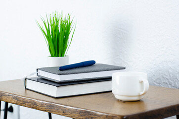 Notepad and books and pen on the table. Desktop. Green flowerpot in a white pot. A cup of coffee. Office.
