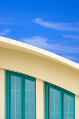 Green glass attic windows on curved roof of modern yellow building against white cloud and blue sky background in vertical frame