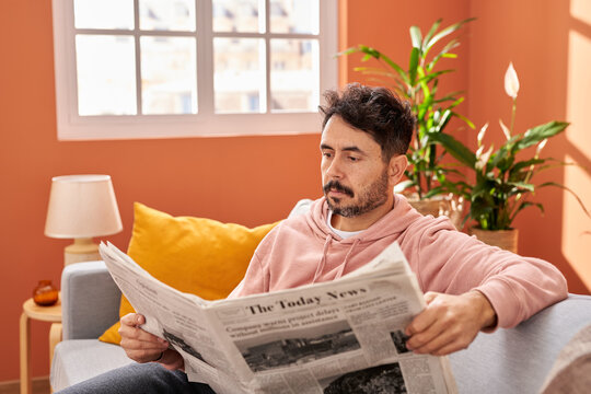 Man in casual wear reading newspaper in living room