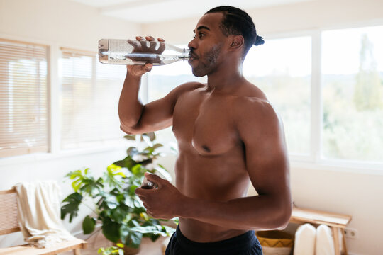 Ethnic muscular sportsman drinking water at home