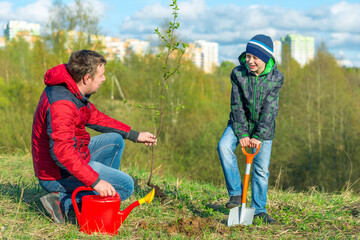 Father and son schoolboy in spring plant a tree shoot in the park concept family, help, care