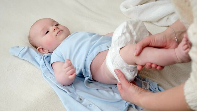 Young mother putting on new clean diapers on her little baby son lying on bed. Concept of parent,baby hygiene and child development
