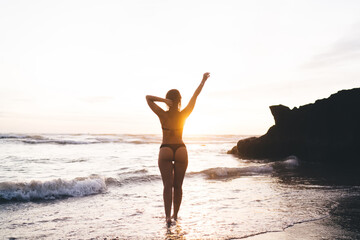Fototapeta na wymiar Slim woman with raised arms standing in waves of ocean