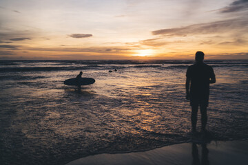 Fototapeta premium Silhouettes of surfers in rippling water of ocean in sunset
