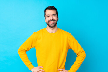 Young caucasian man over isolated blue background posing with arms at hip and smiling