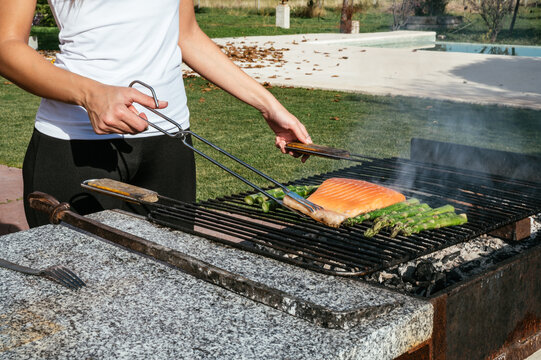 Unrecognizable person frying fish and asparagus on grill grate