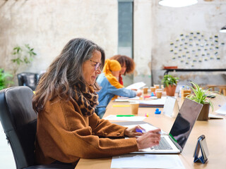 Mature female worker analyzing data on laptop