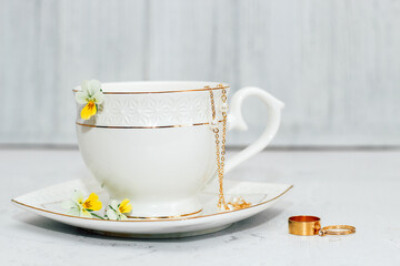 A beautiful white cup with a gold border, decorated with flowers and gold jewelry. Business account design.