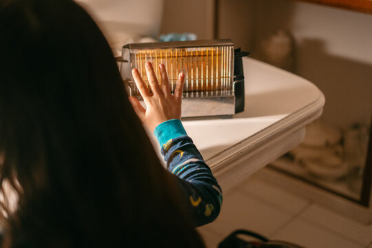 Kid warming his hands in a bread toaster at kitchen