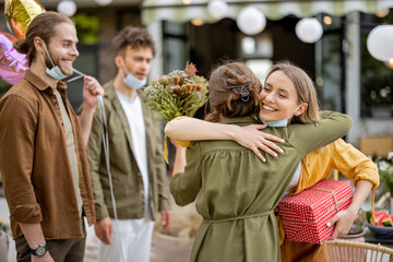 Young adult friends gathering for birthday party at backyard of the house outdoors. Happy to greet and embrace each other after the pandemic