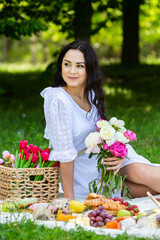 Beautiful brunette woman resting in park sitting on a picnic blanket. Relaxing in nature.