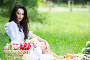 Beautiful brunette woman resting in park sitting on a picnic blanket. Relaxing in nature.