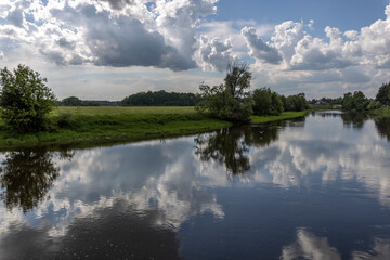 Fototapeta na wymiar River with blue sky and clouds reflected in the water on a summer day. Two seagulls are flying over the river