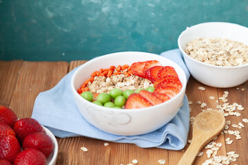 Oatmeal with strawberries, in a bowl on a wooden table background. Healthy breakfast food