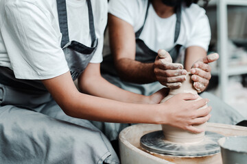 A girl and a man in aprons in a clay workshop. Male and female hands make clay vases