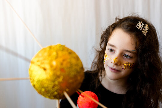 Portrait of little girl observing her solar system project with glitter on her face
