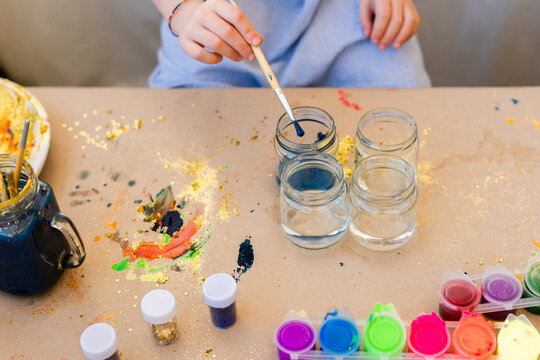 top view of girl making crafts with colored paints and glitter