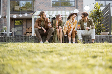 Group of young friends spending summertime together, having fun while sitting in a row on a porch...