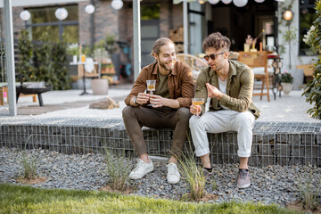 Two male friends having a close conversation, sitting with drinks on a porch of the country house outdoors. Fun summer time in a country house, male friendship
