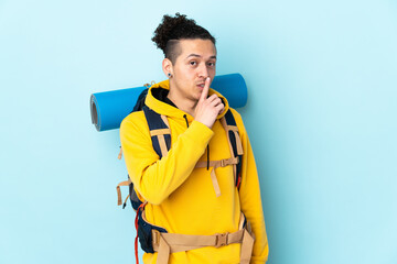 Young mountaineer man with a big backpack over isolated blue background doing silence gesture