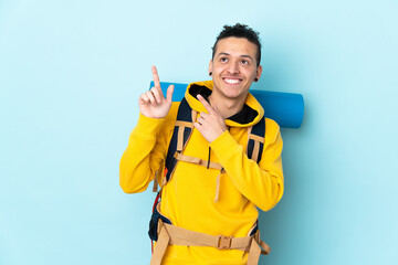 Young mountaineer man with a big backpack over isolated blue background pointing with the index finger a great idea