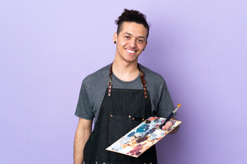 Young artist man holding a palette over isolated purple background smiling a lot