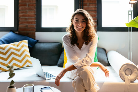 Cheerful female freelancer sitting on couch near laptop