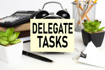 delegate tasks. the inscription on the sticker on the alarm clock near the calculator and flowerpots