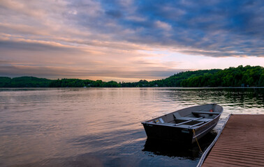 A small, empty rowboat is docked in a calm, quiet lake during a beautiful sunset in Muskoka, Ontario.