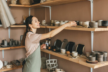 Young woman arranging goods in pottery workshop. Creative people and hobby concept.