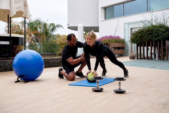 Woman balancing on ball and coach assisting