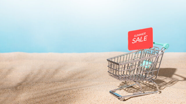 Shopping trolley cart on beach sand with red sale tag. Summer sale concept. Summer shopping.