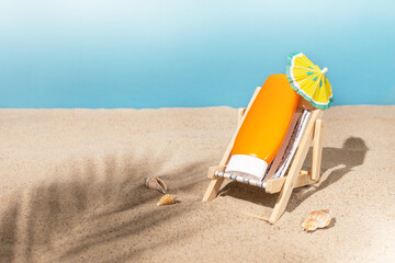 Creative composition with sunscreen on a toy deckchair on sand with seashells and palm leaf shadow....