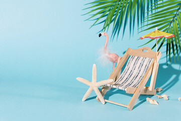 Fototapeta na wymiar Creative composition with beach accessories, such as deckchair, beach umbrella, seashells, pink flamingo and palm leaf on blue background. Summer vacation concept. Summer background.