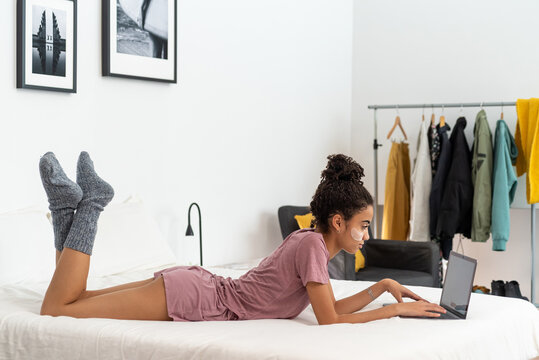 African American teen with under eye patches browsing laptop on bed