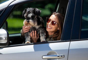 Young woman looking out car window holding schnauzer dog smiling,