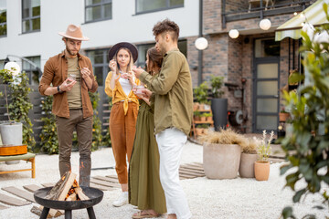 Group of young friends hang out by a fireplace, preparing for grilling at the backyard. Barbecue in close company near a country house