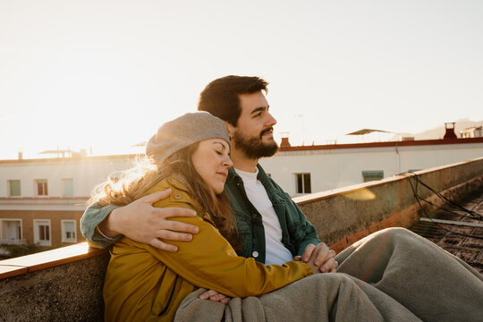 Loving ouple sitting on rootop and hugging during sunset
